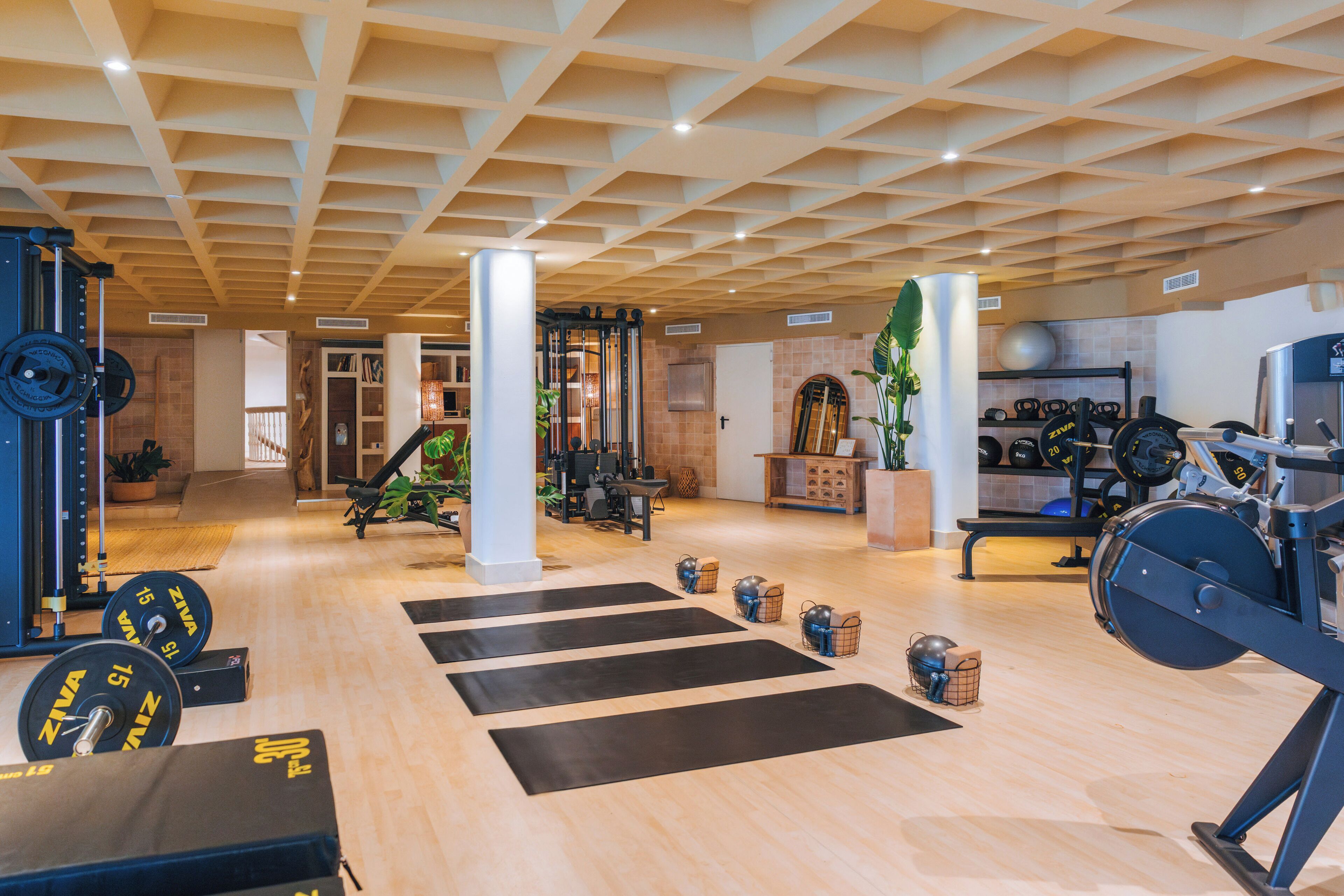 Un gimnasio con equipo de levantamiento de pesas, colchonetas de ejercicio y un techo con diseño geométrico.