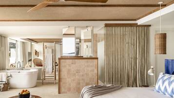 Habitación de hotel moderna con una cama grande, una bañera, una zona de estar con una silla y vistas al exterior.