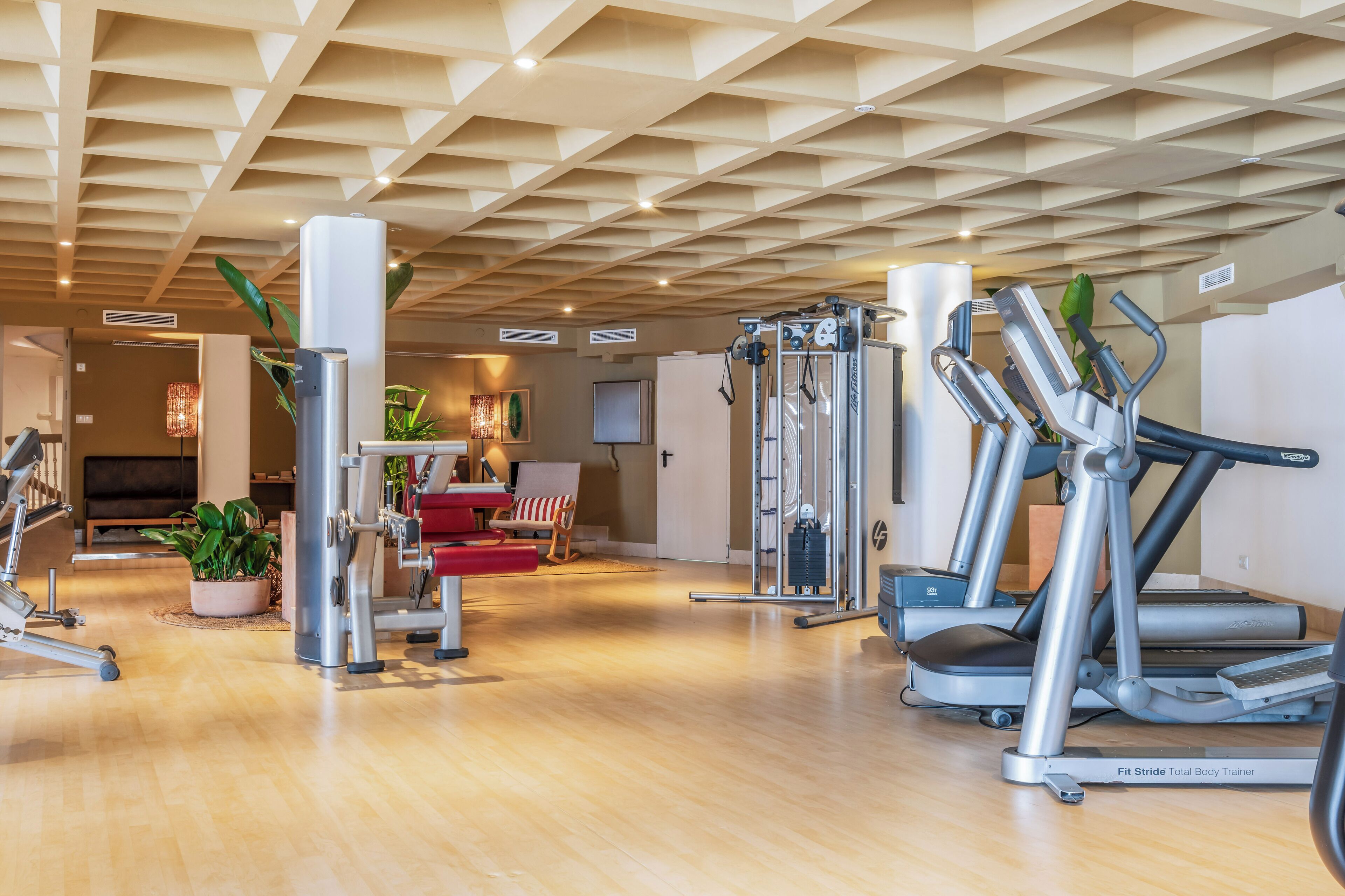 Un gimnasio con diversos equipos de ejercicio, incluyendo cintas de correr y máquinas de pesas, y piso de madera.