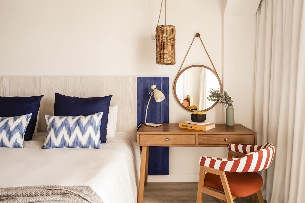 A bedroom with a bed, a desk, a chair, a lamp, a mirror, and a hanging light fixture.