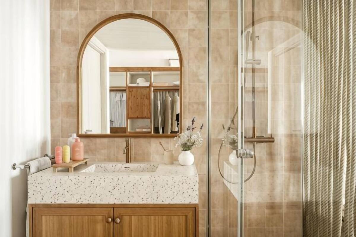 A bathroom with a freestanding mirror, a sink with a speckled countertop, and a shower with a glass door.