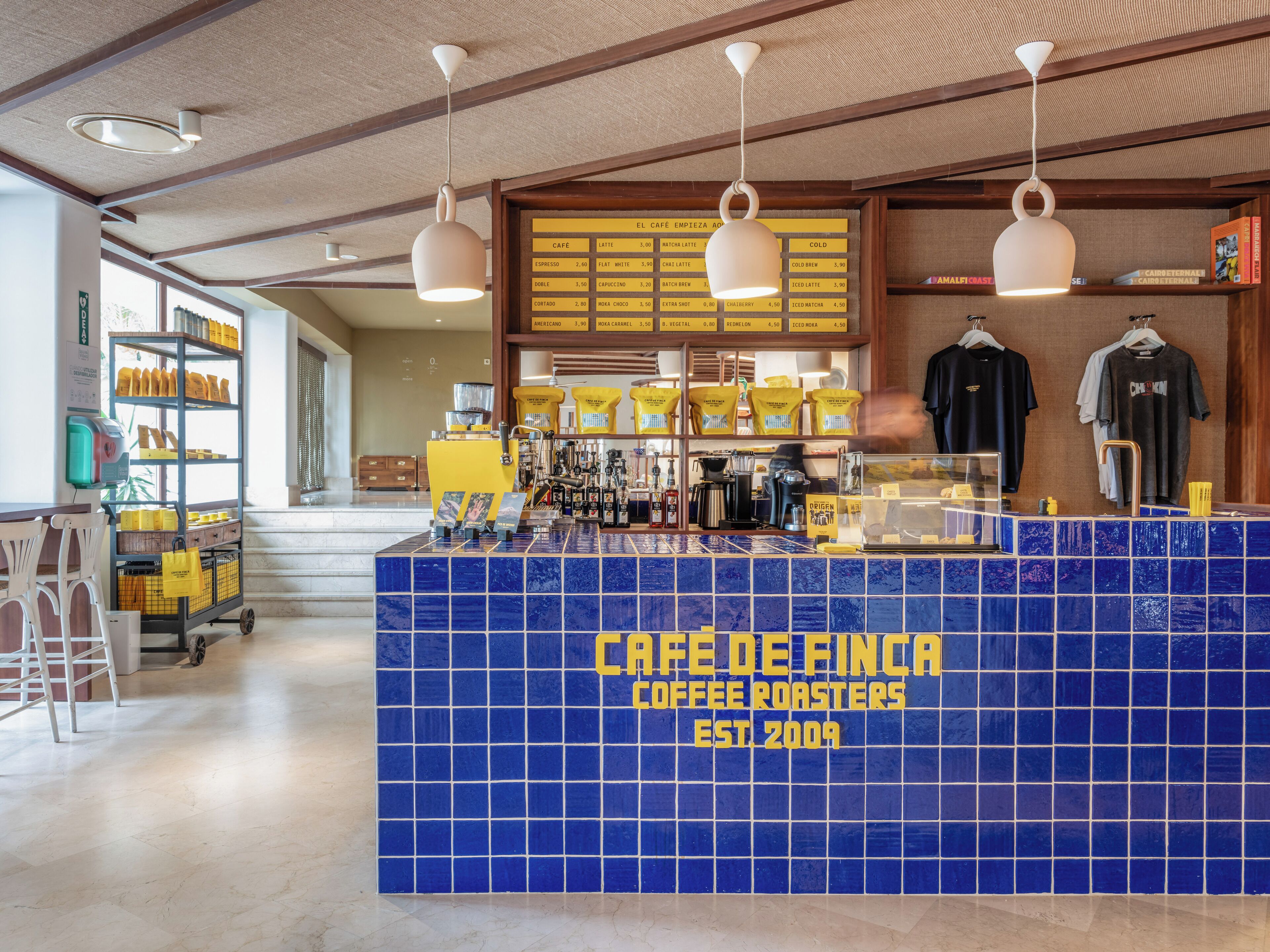 A coffee shop counter with a blue tiled front, a menu board above, and hanging lights.