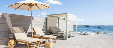 A deck with two lounge chairs and a canopy umbrella, overlooking a body of water with boats.