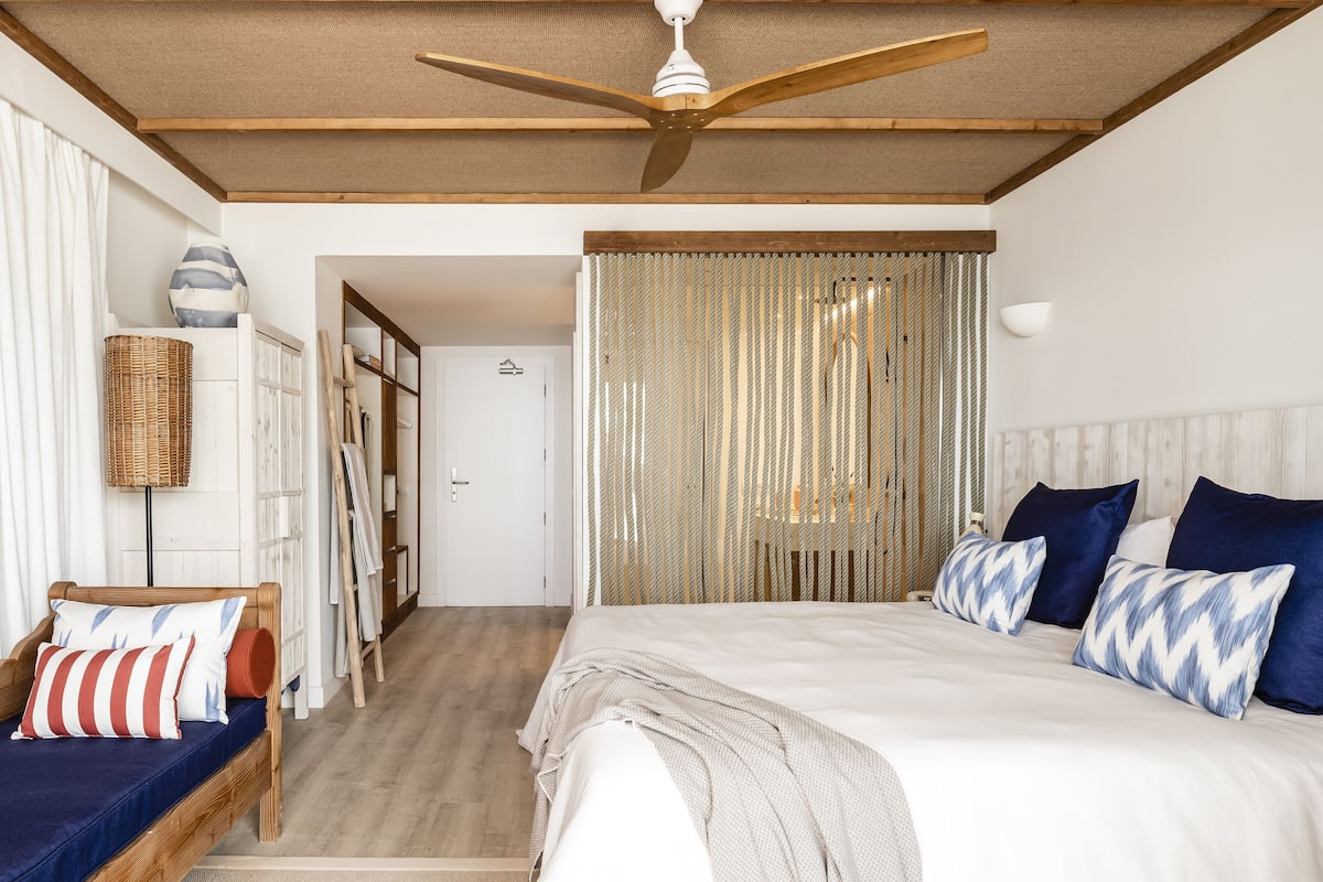 A bedroom with a bed, a ceiling fan, a wicker basket, and a door leading to another room.