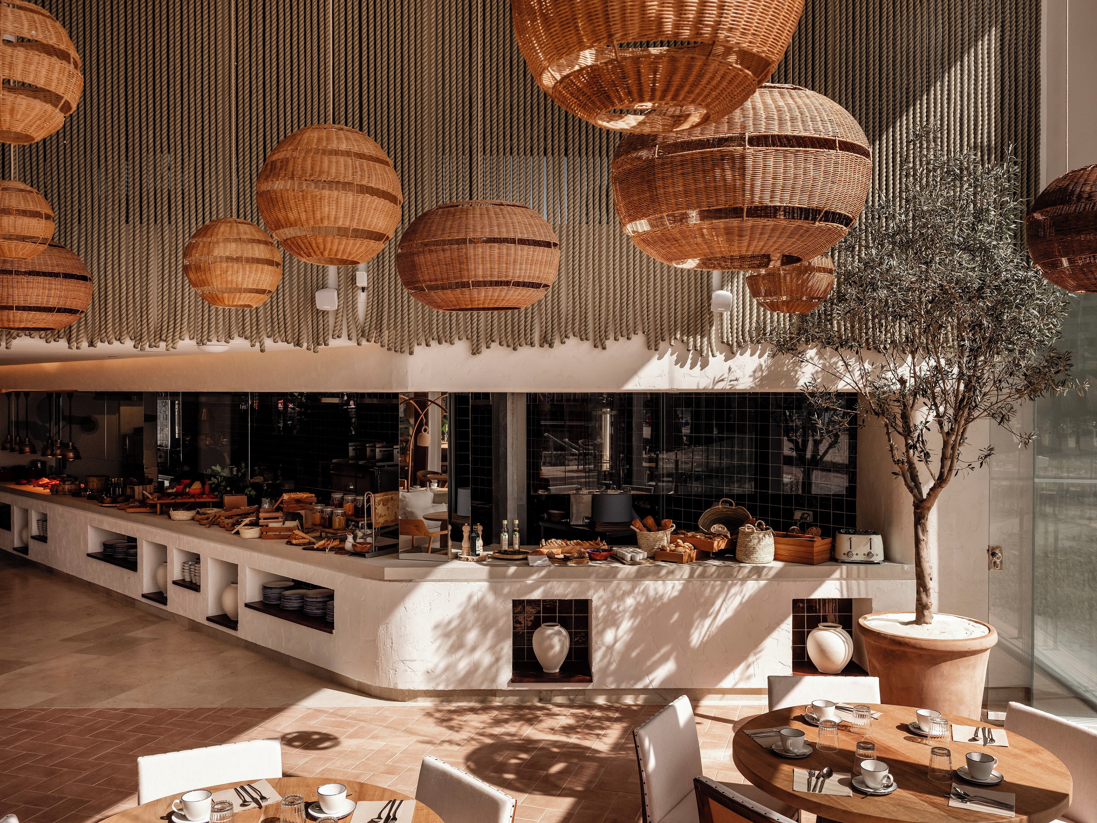 Un restaurant moderne avec un long comptoir, des suspensions en osier et un grand arbre en pot.