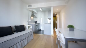 A modern living room with a grey sofa, a dining table with chairs, and a kitchen area in the background. - Hotel Jauregui (Hondarribia)