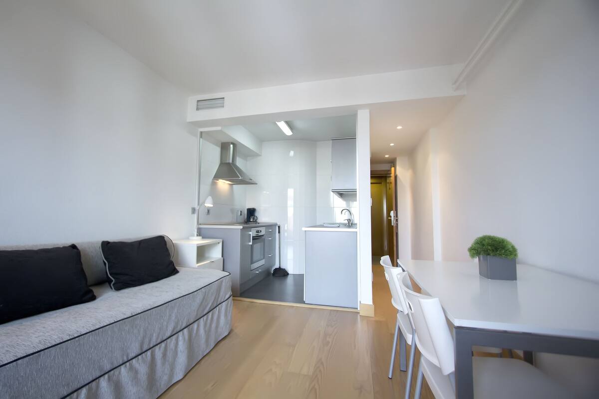 A modern living room with a grey sofa, a dining table with chairs, and a kitchen area in the background.