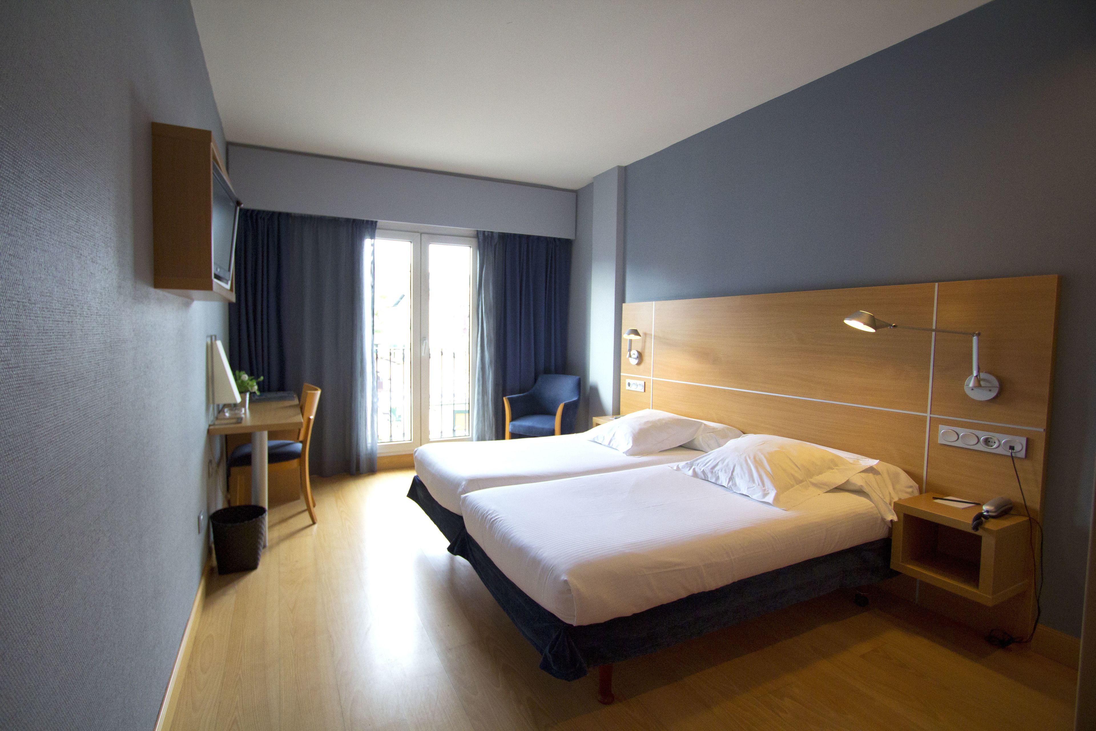 A hotel room with two beds, a desk, a chair, and a small table.