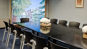 A conference room with a long table, six chairs, and a large window with a scenic view of buildings and trees. - Hotel Jauregui (Hondarribia)