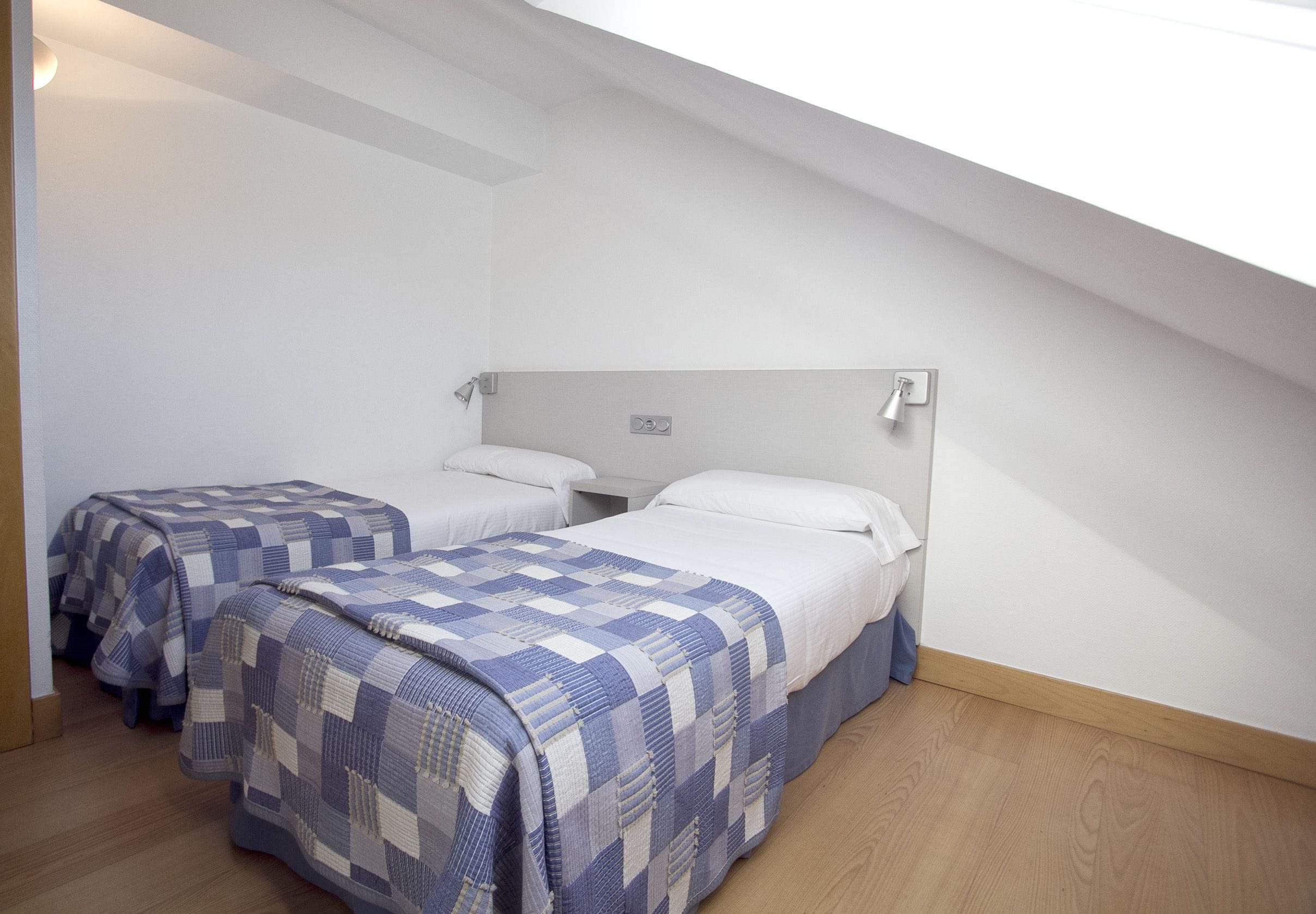 Un dormitorio con dos camas individuales, cada una con una manta a cuadros, suelo de madera y techo inclinado.