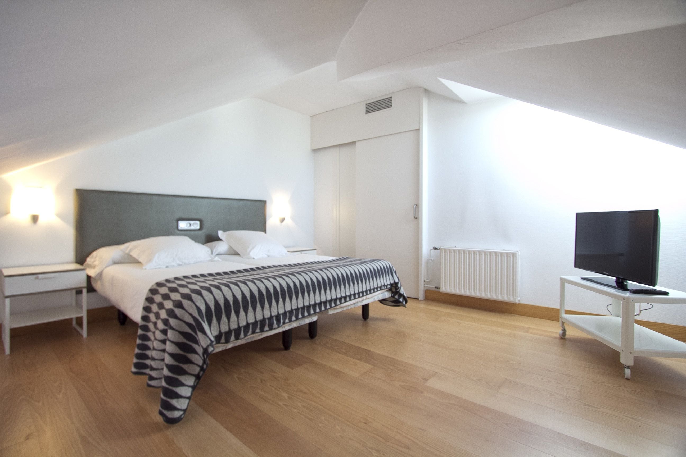 Quarto de hotel moderno com uma cama grande, televisão e escrivaninha.