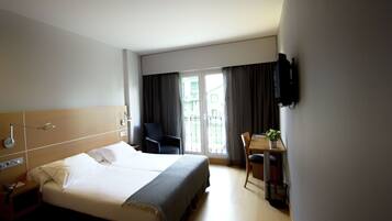 Una habitación de hotel con una cama grande, un escritorio, una silla, un televisor y una ventana con cortinas.