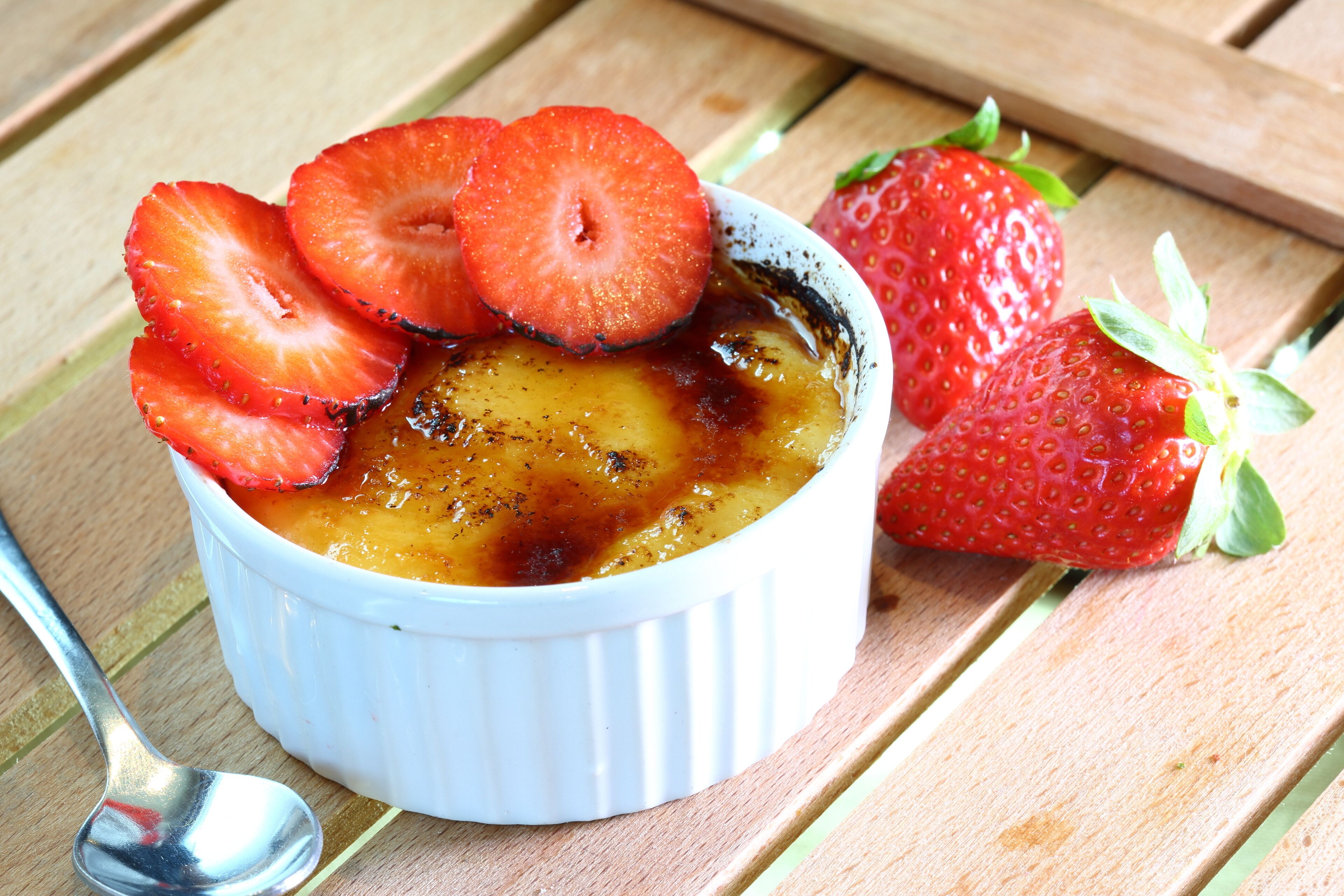 A dessert in a white ramekin with strawberries on top, placed on a wooden surface.