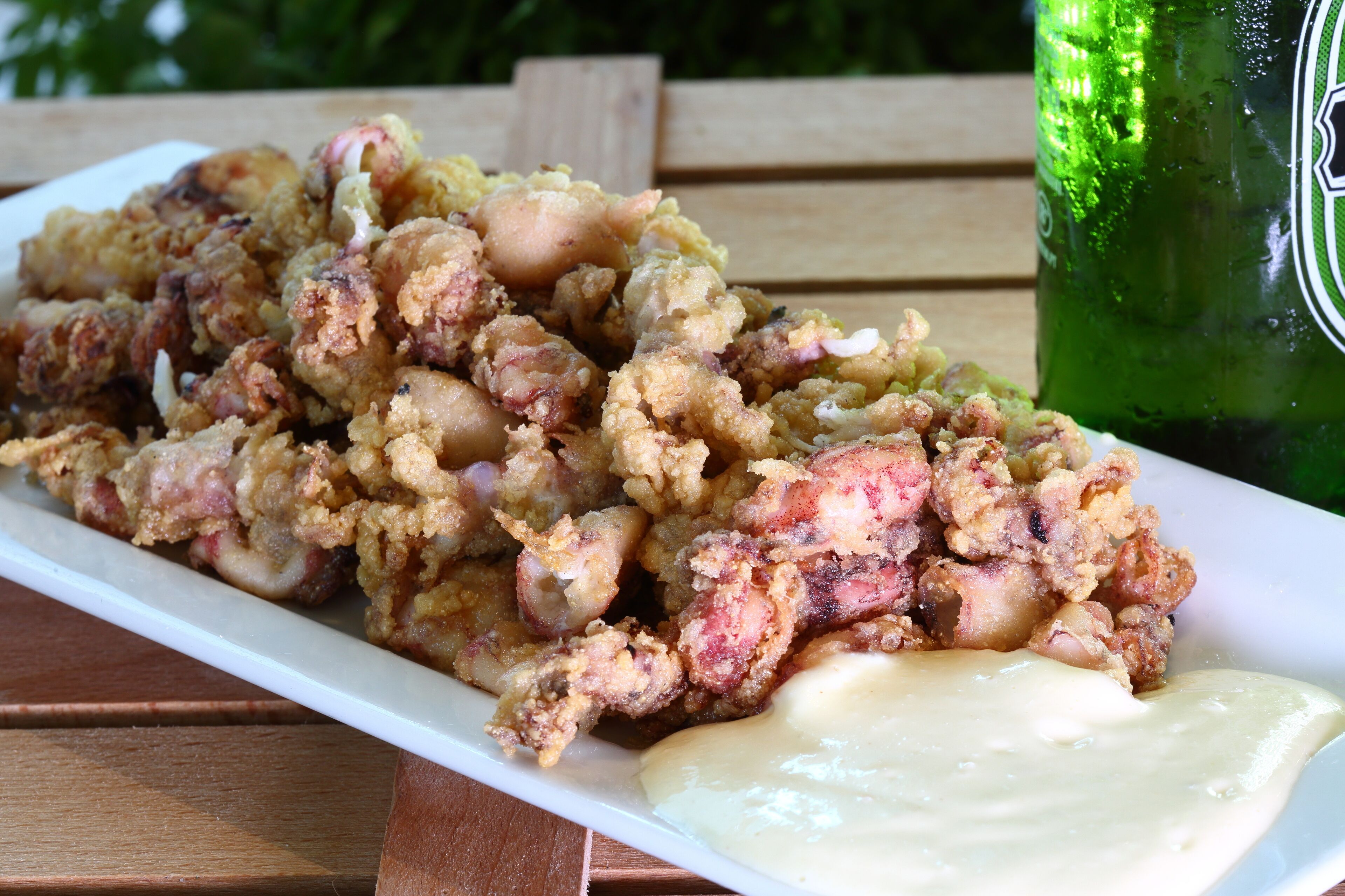 Un plato de comida frita con salsa cremosa, una botella verde y una mesa de madera.