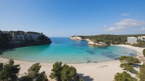Un paisaje costero con playa arenosa, aguas turquesas cristalinas y acantilados rocosos.