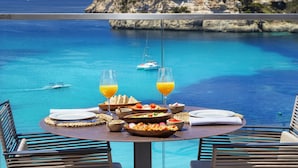 Mesa lista para el desayuno con vista al mar y una isla rocosa.