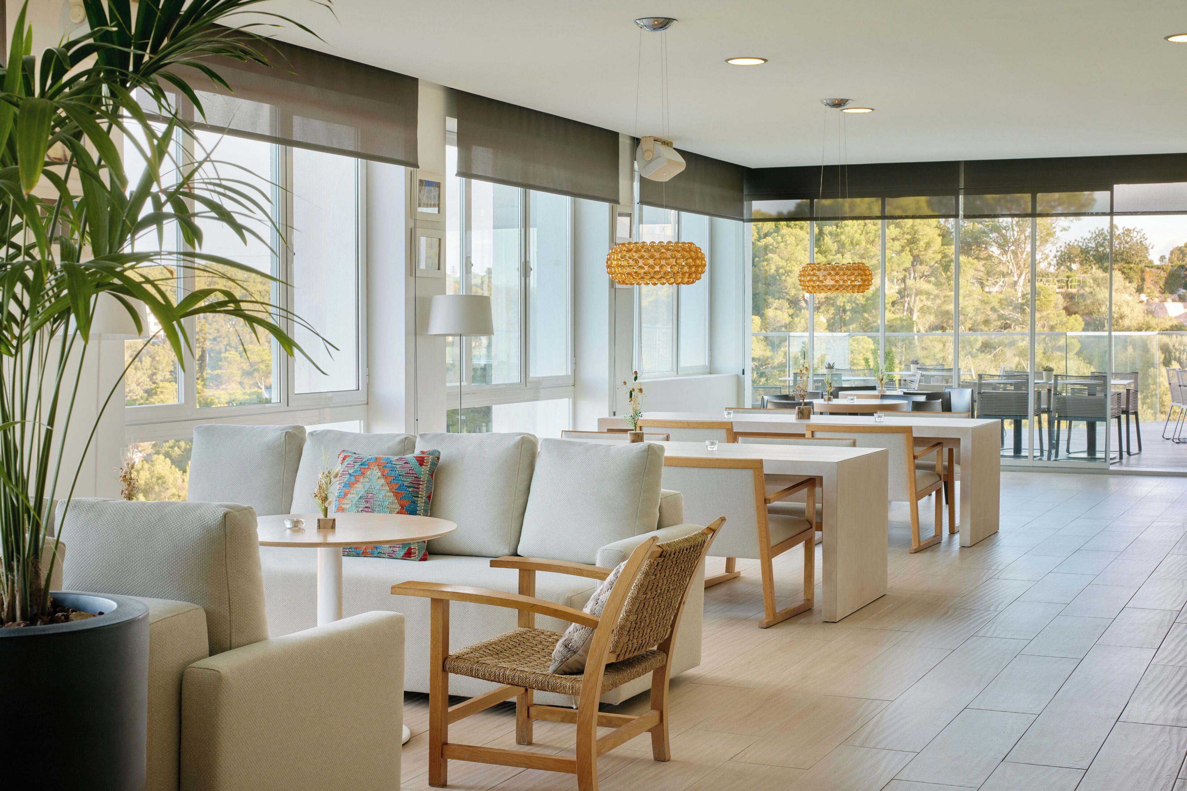 Een modern interieur met een bank, stoelen, een tafel en een groot raam met uitzicht op bomen.