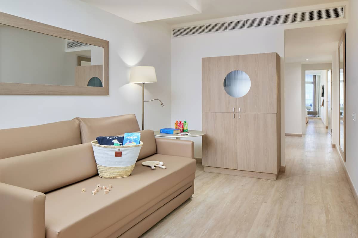 Ein modernes Hotelzimmer mit einem beigefarbenen Sofa, einem runden Spiegel, einem kleinen Tisch mit Lampe und einem Kleiderschrank.