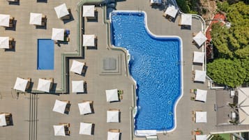 Une vue aérienne d’une piscine entourée de chaises longues et de parasols, avec une petite piscine adjacente et un espace abrité.