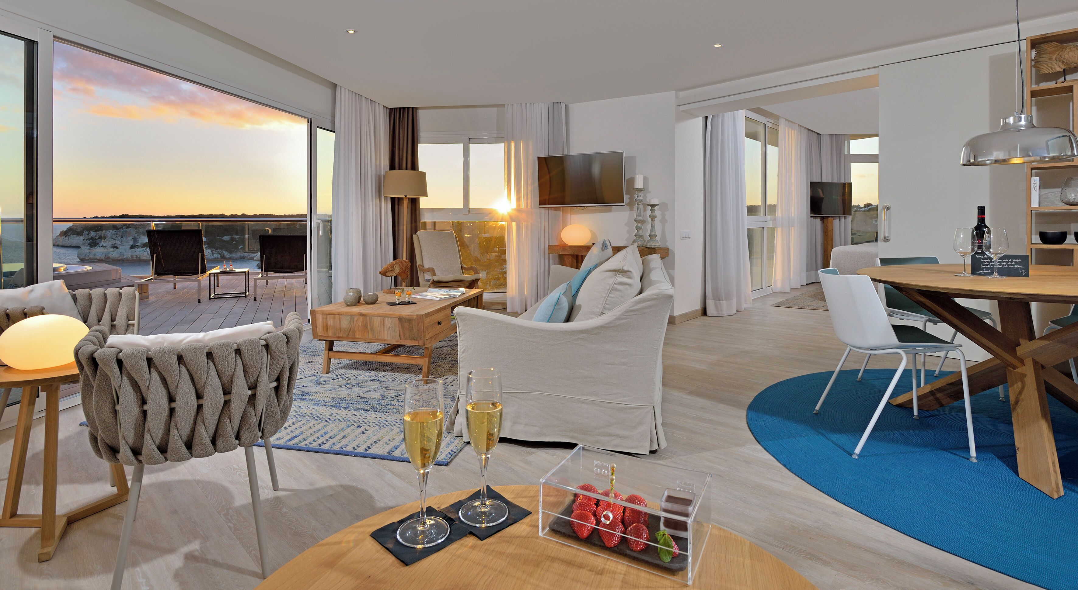 Una habitación de hotel moderna con un ventanal grande, un sofá, una mesa de comedor y un televisor.