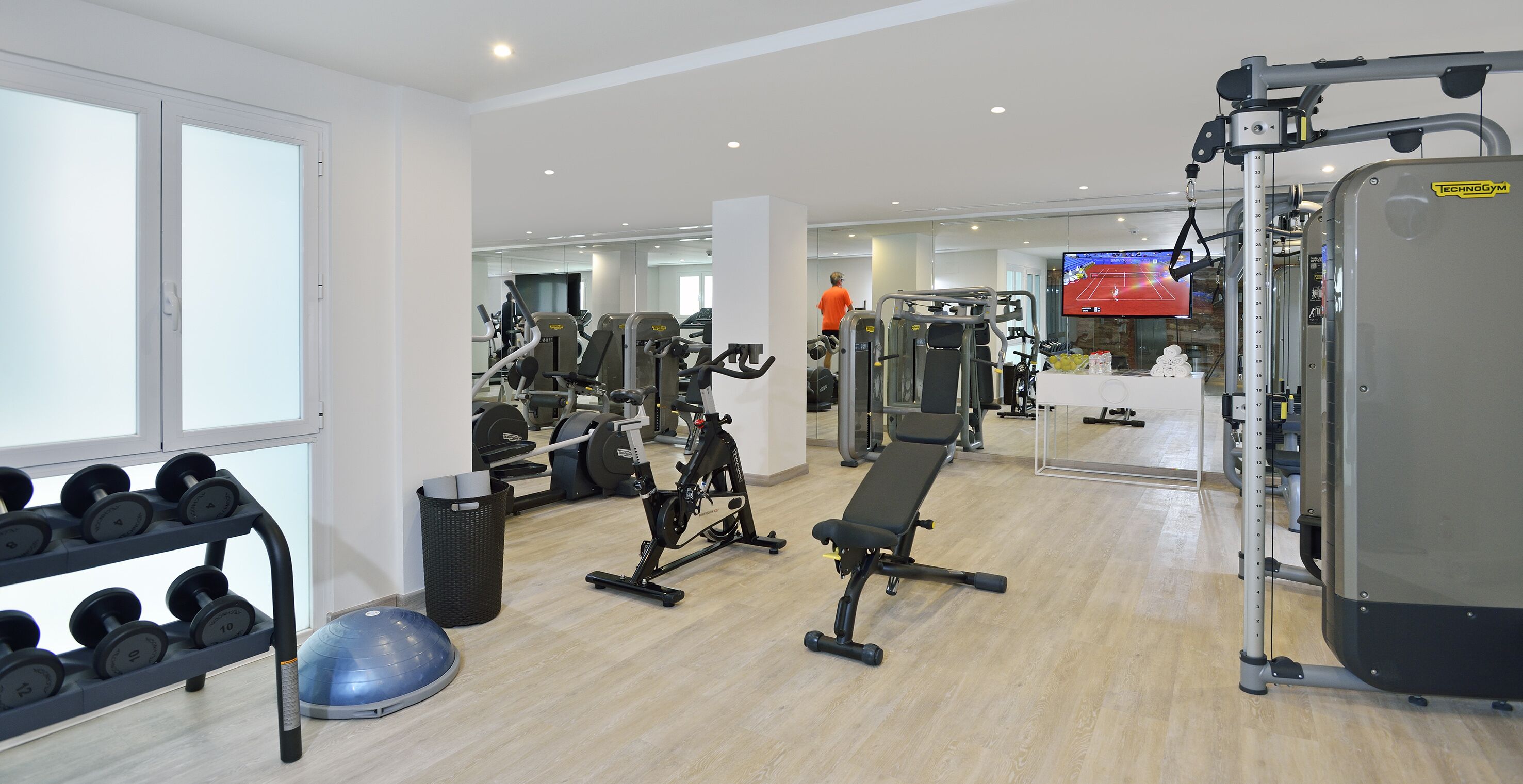 Un gimnasio con equipo de ejercicio, una banca y una pantalla de televisión.