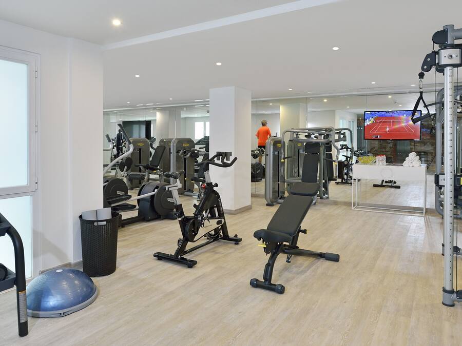 Un gimnasio con equipo de ejercicio, una banca y una pantalla de televisión.