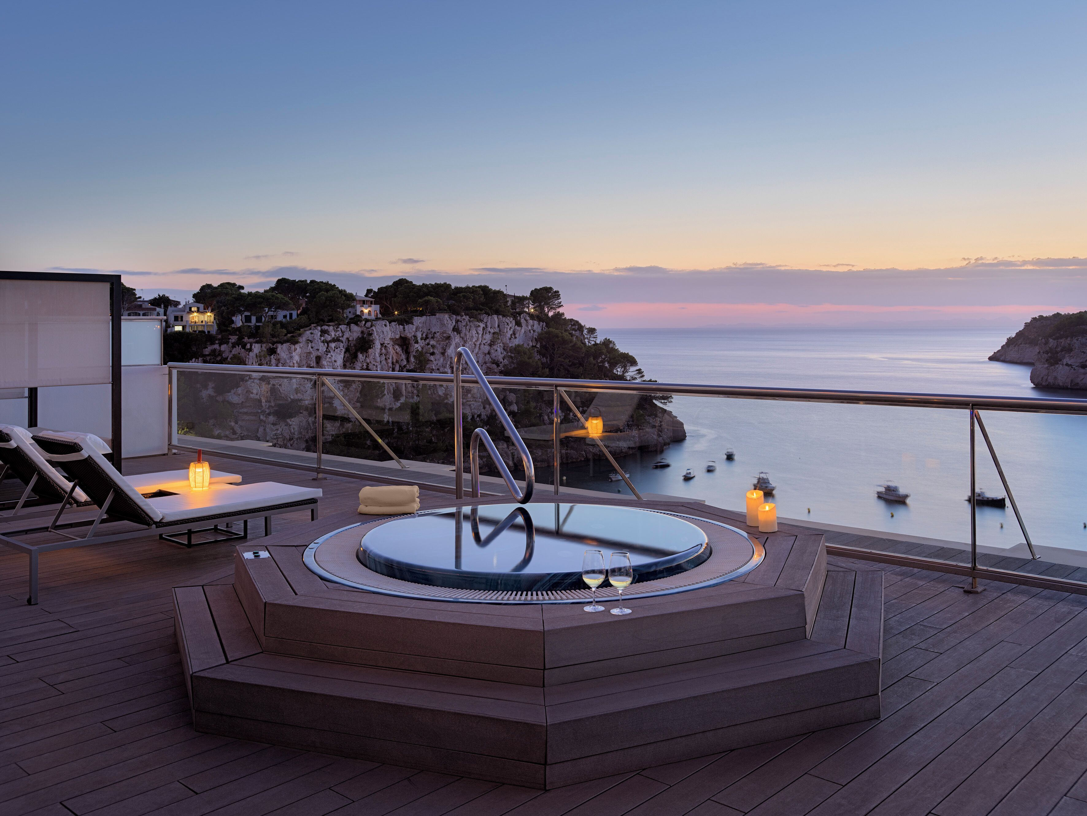 A hot tub on a deck with a view of the sea and cliffs.