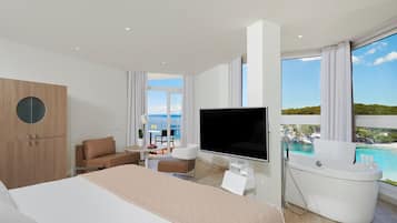 Habitación de hotel moderna con una cama grande, un televisor de pantalla plana, una bañera y un balcón con vista al mar.