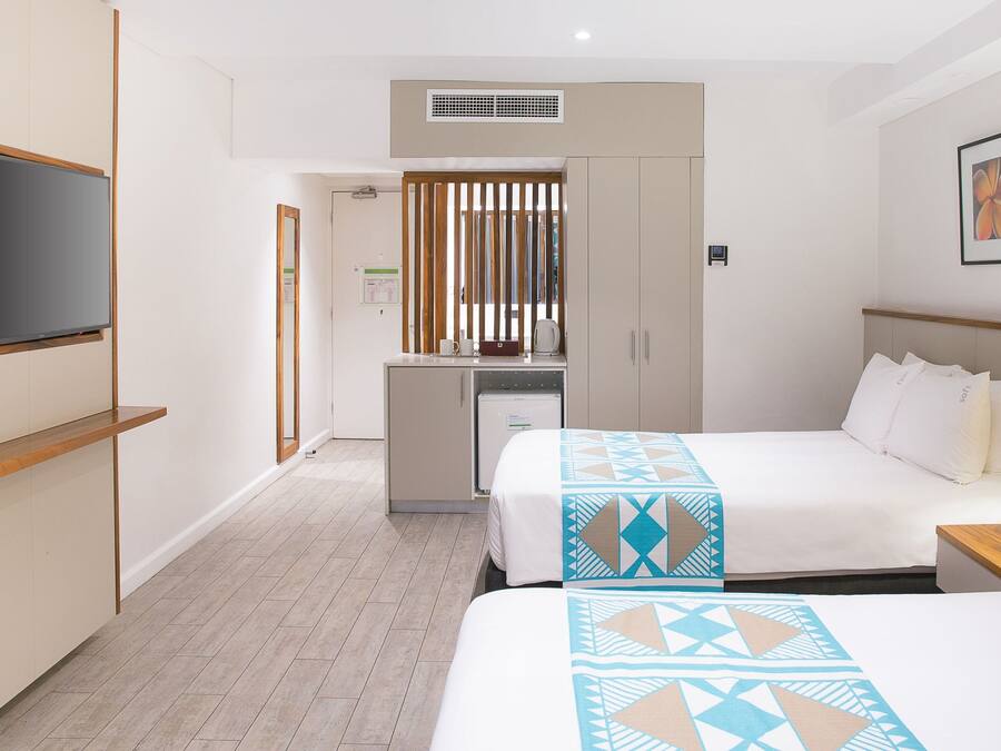 Habitación de hotel con dos camas, un televisor, un escritorio con hervidor y un cuadro en la pared.
