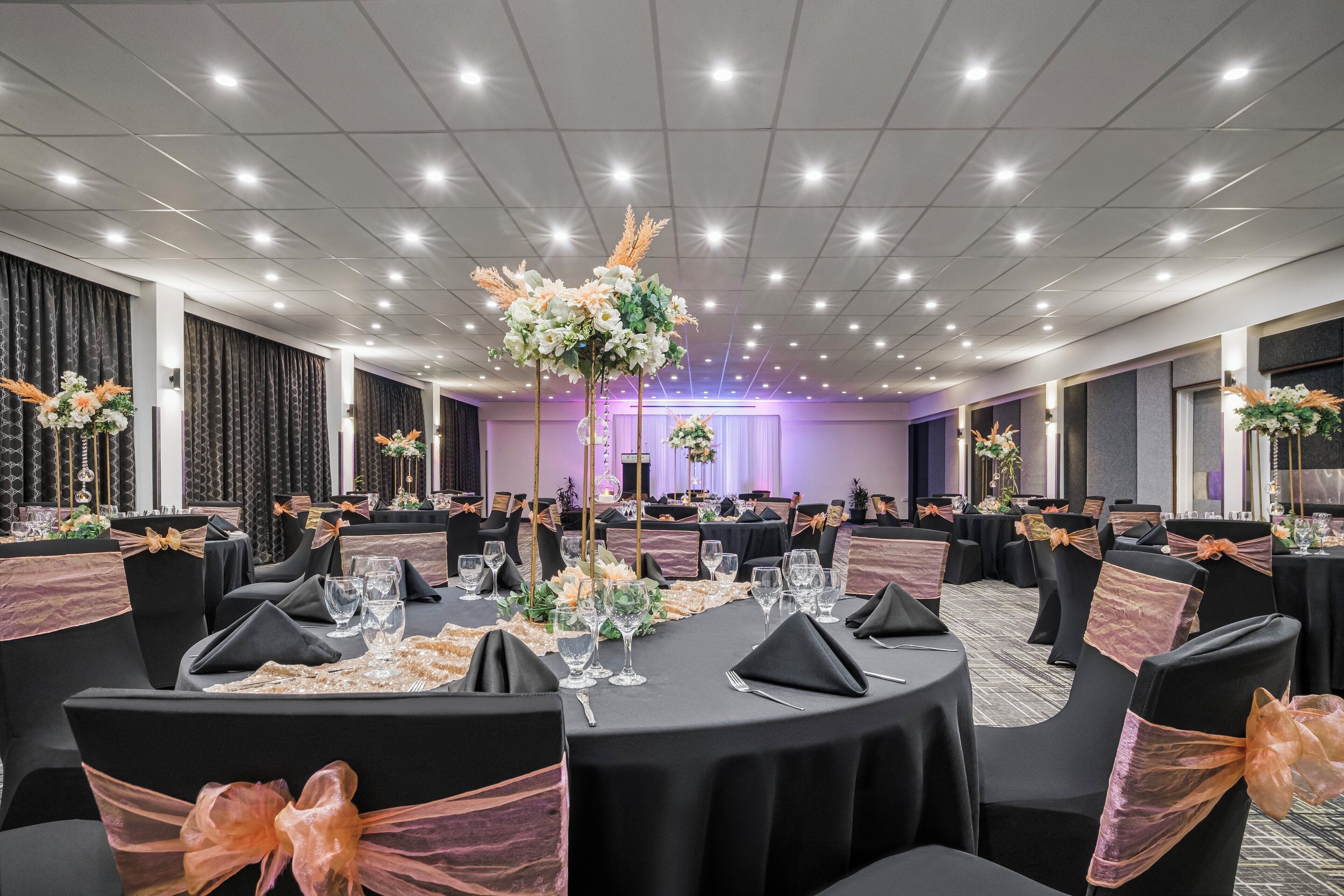 Un salón de banquetes con mesas redondas, sillas negras con cintas naranjas y centros de mesa florales.