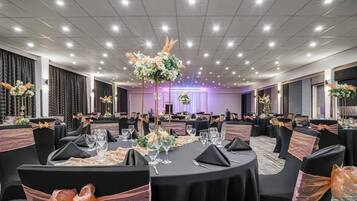 Un salón de banquetes con mesas redondas, sillas negras con cintas naranjas y centros de mesa florales.