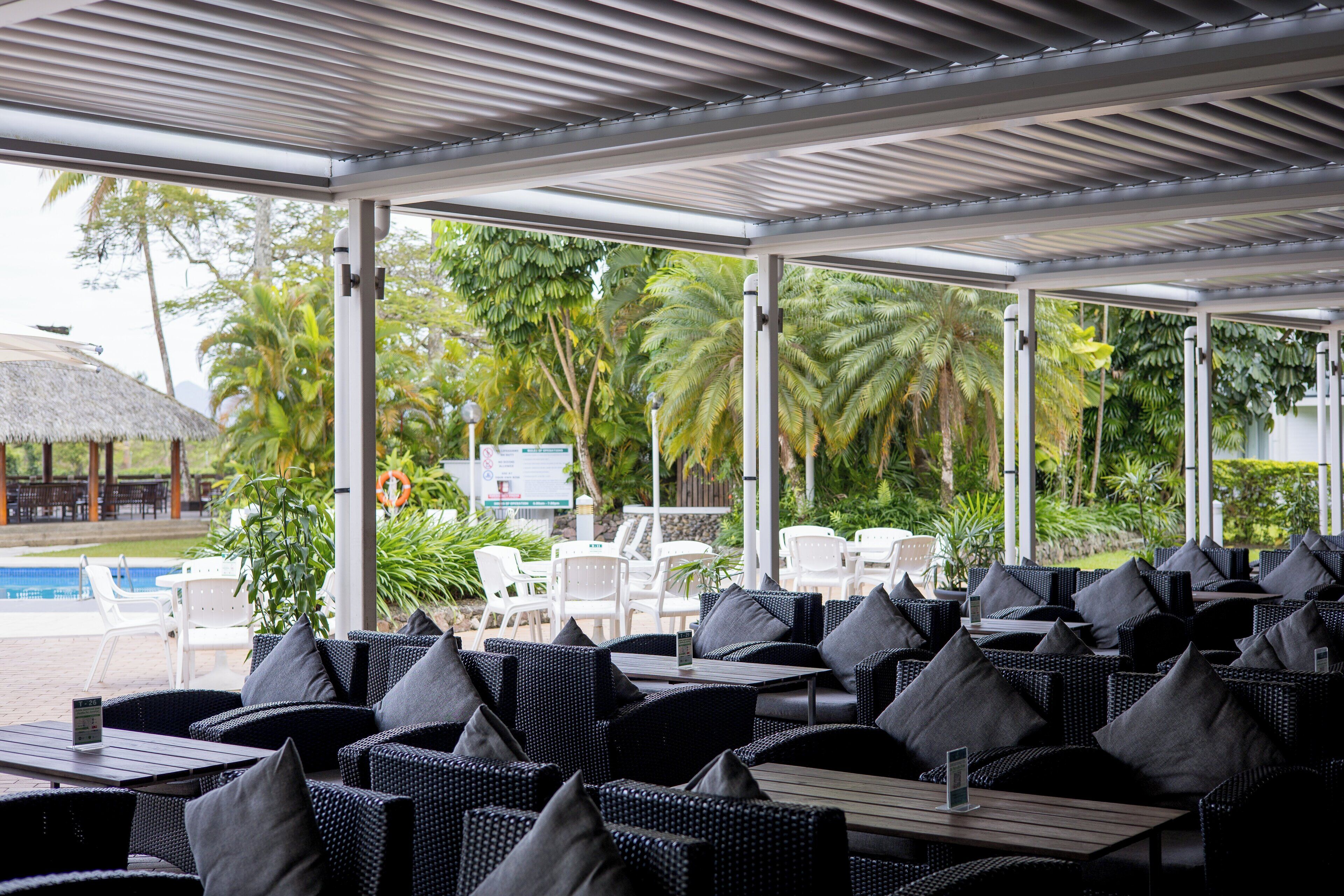 Un espace extérieur aménagé avec des meubles en osier et des chaises blanches, offrant une vue sur une piscine et une végétation luxuriante.