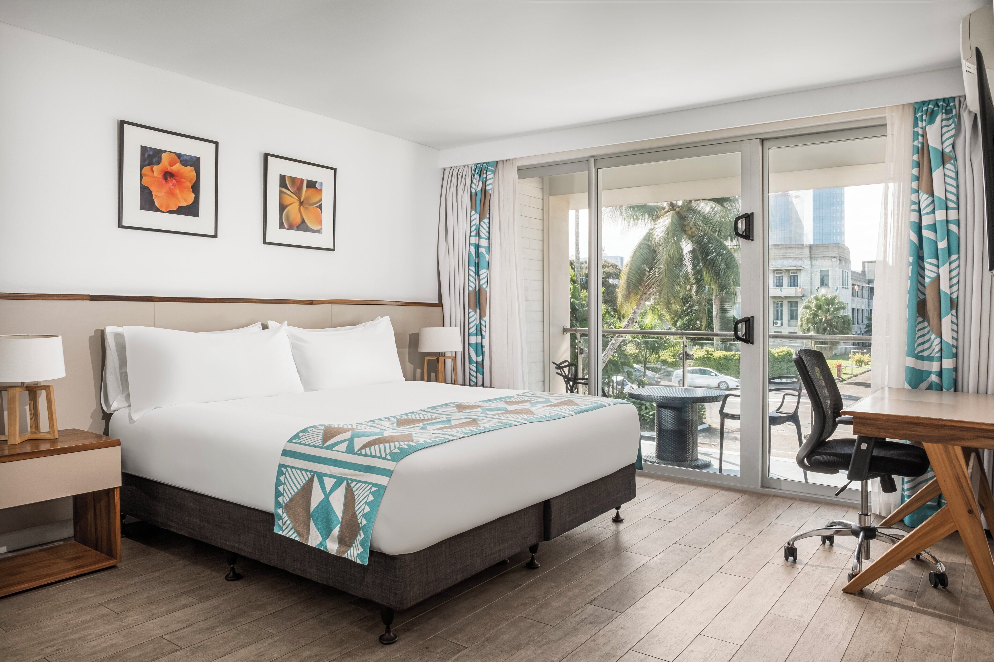 A hotel room with a bed, a desk, a chair, and a balcony with a view of the city.