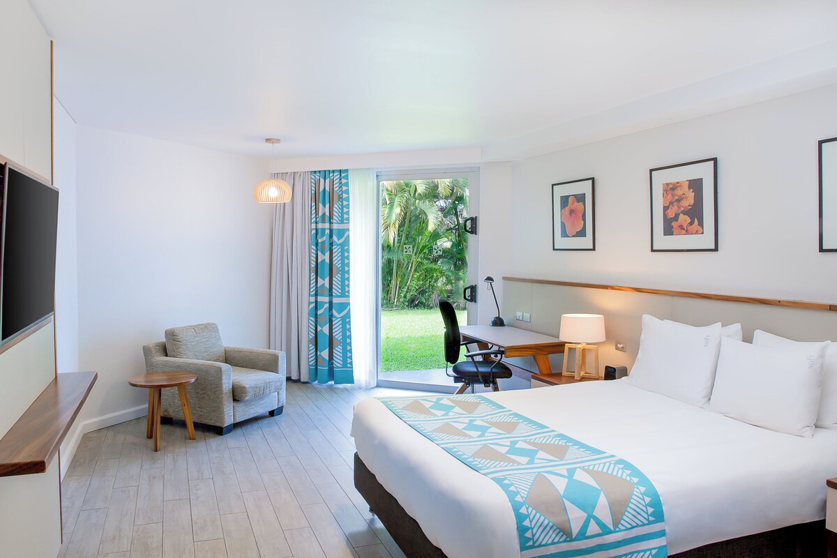 Habitación de hotel con cama, escritorio, silla, televisor y vistas al exterior.