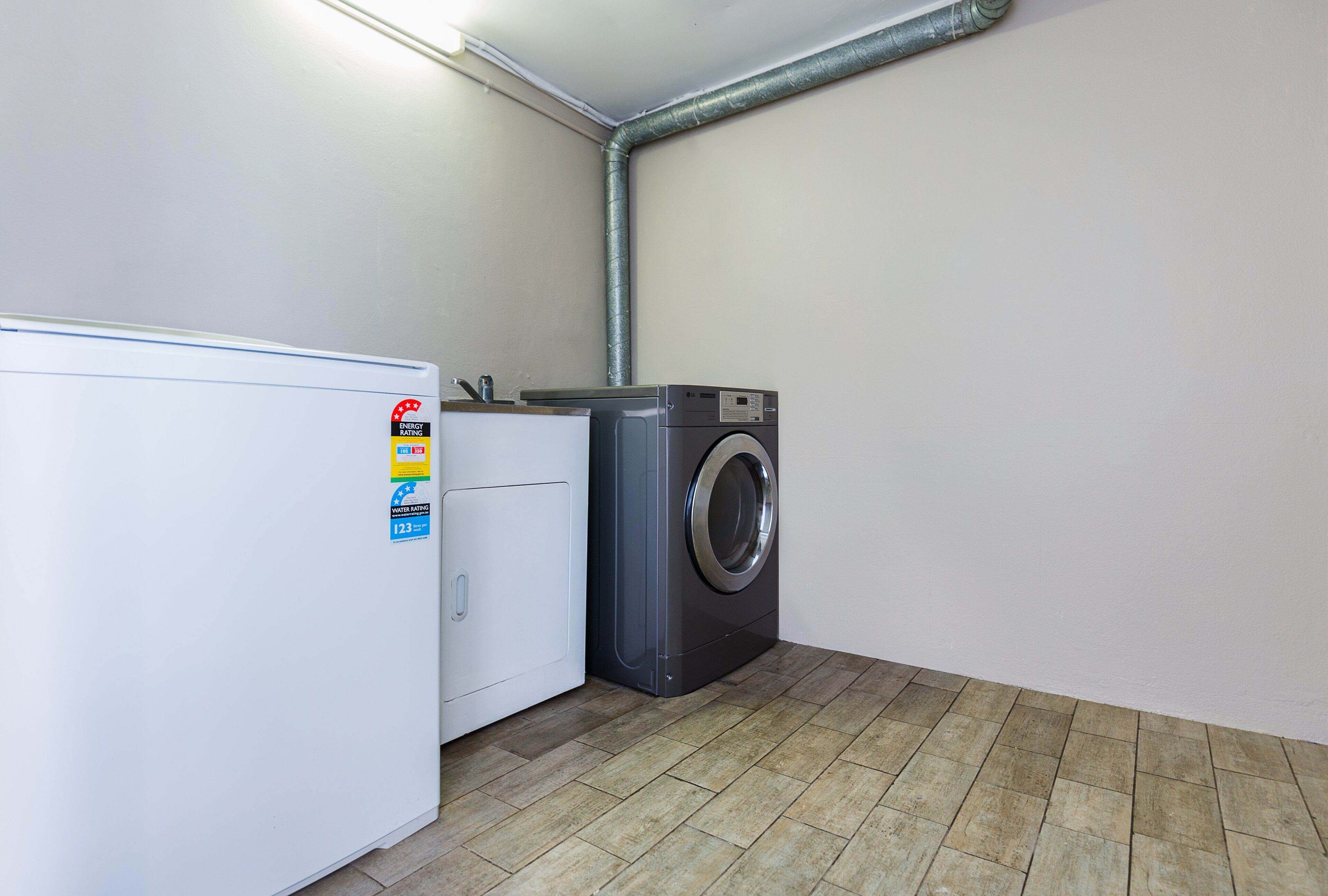 A laundry room with a white washing machine and dryer, a tiled floor, and a visible duct running along the wall.