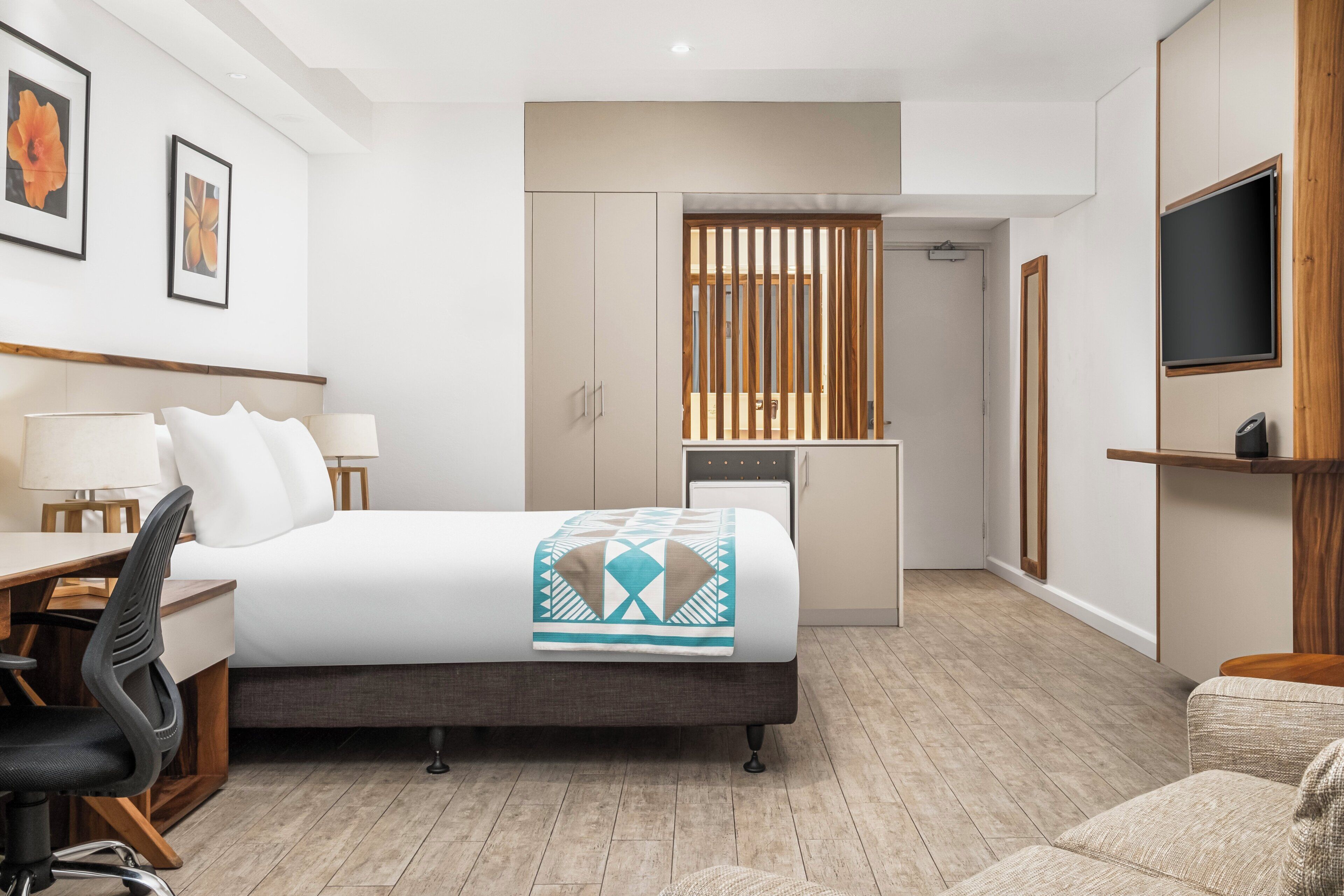 A hotel room with a bed, desk, chair, and a small kitchenette area.
