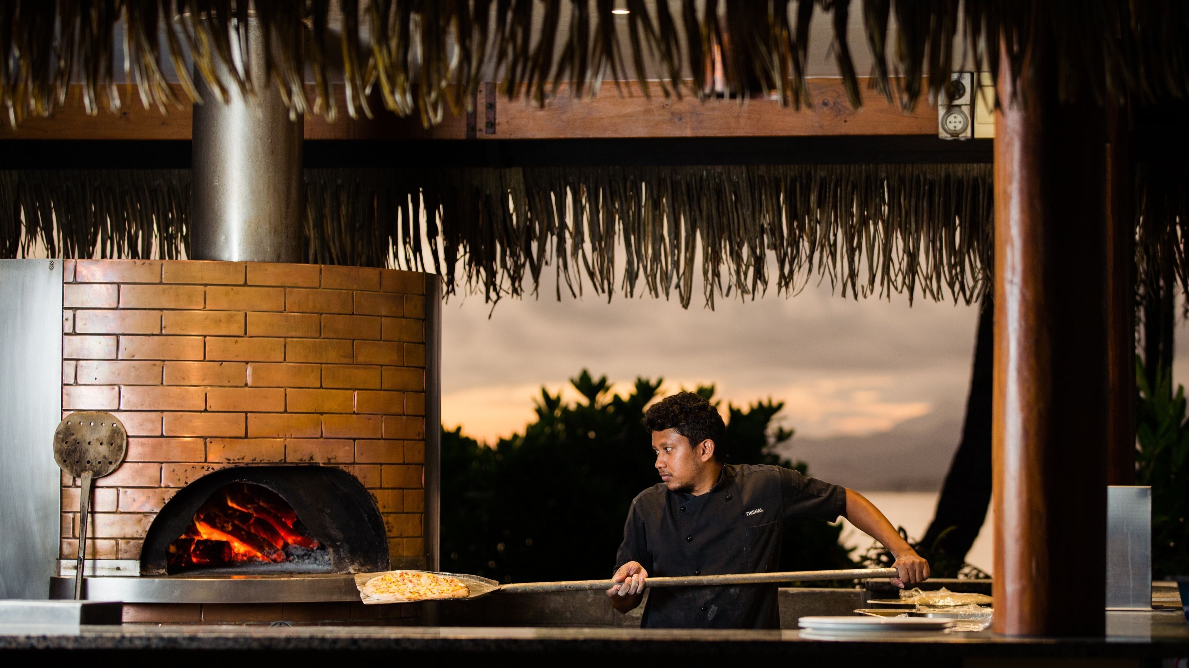 A brick oven pizza oven with a person using a long-handled tool to manage a pizza.