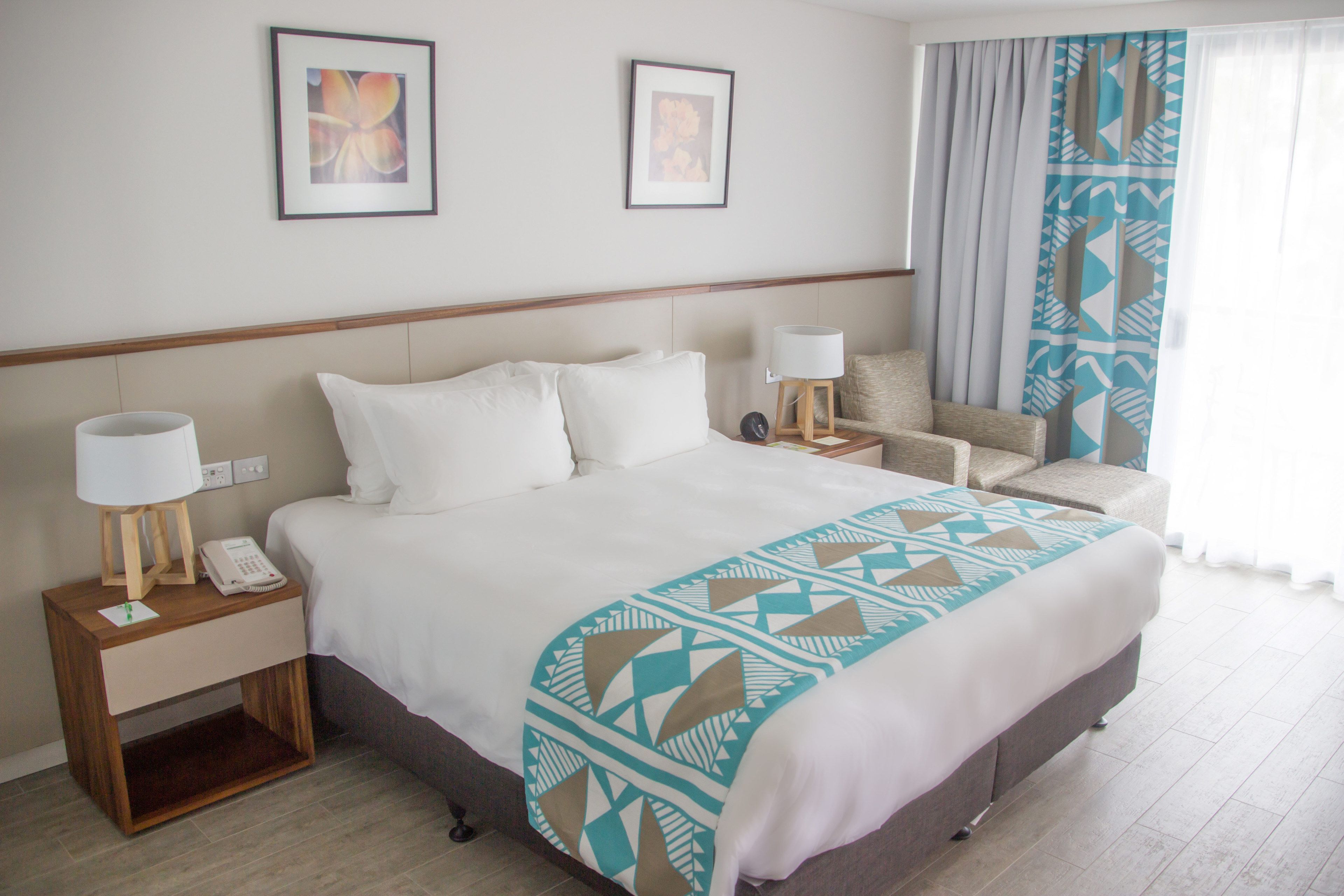 A hotel room with a large bed, two bedside tables with lamps, a chair, and a window with curtains.