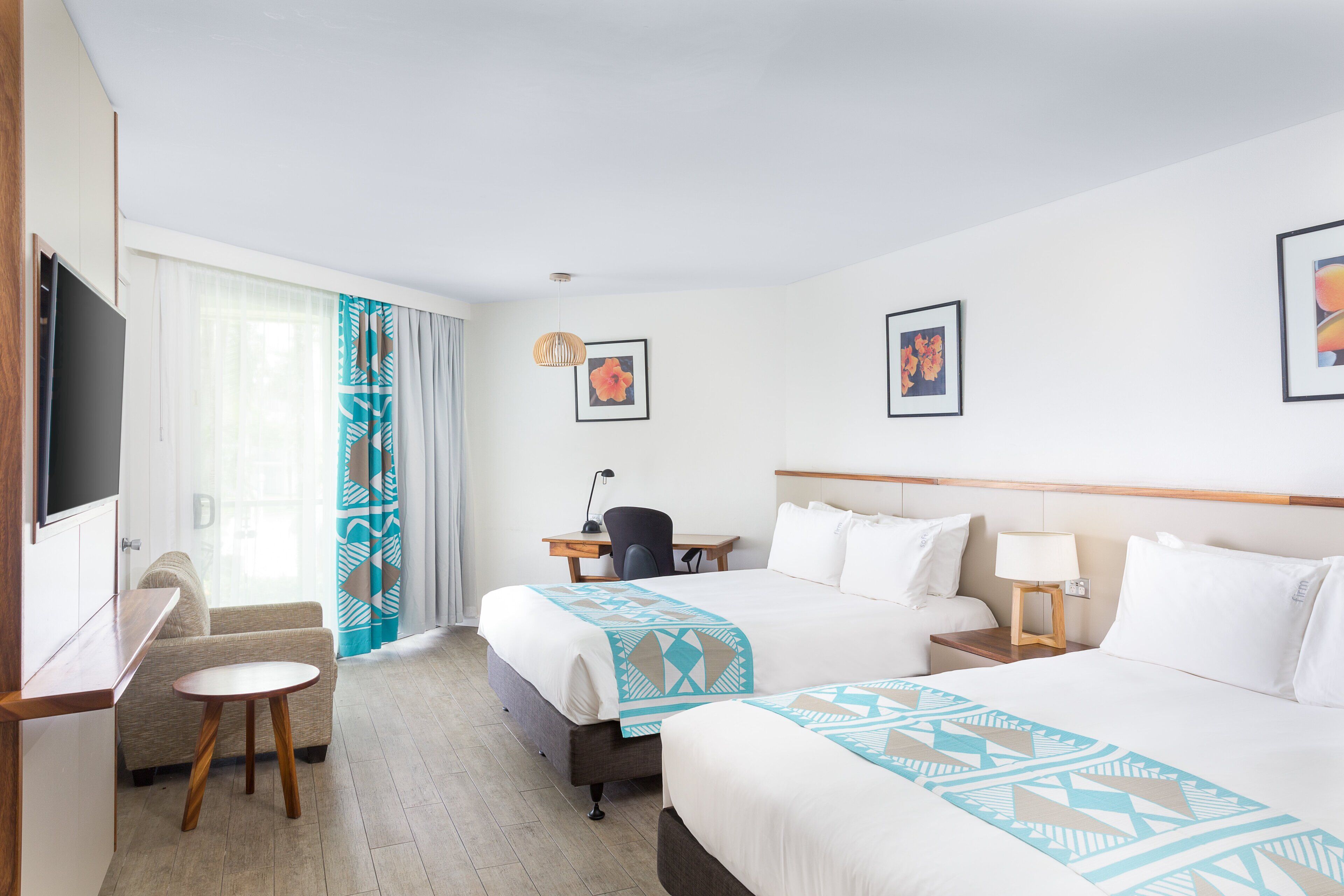 A hotel room with two beds, a desk, a chair, a TV, and artwork on the walls.