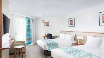 A hotel room with two beds, a desk, a chair, a TV, and artwork on the walls.