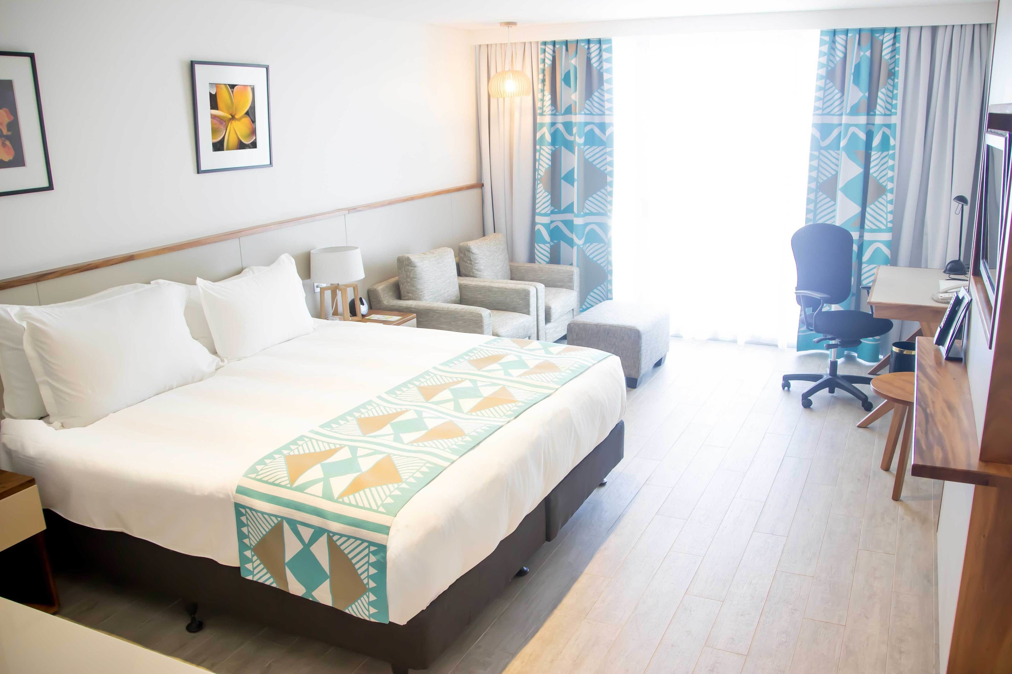 A hotel room with a large bed, a desk, a chair, and a television.