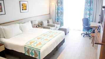 A hotel room with a large bed, a desk, a chair, and a television.