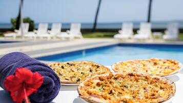 Three pizzas on a table near a pool with lounge chairs in the background.