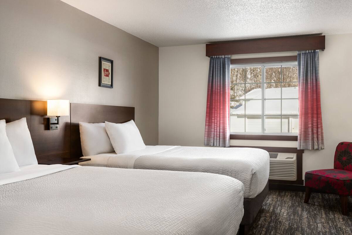 Een hotelkamer met twee bedden, een nachtkastje, een lamp, een stoel en een raam met gordijnen.