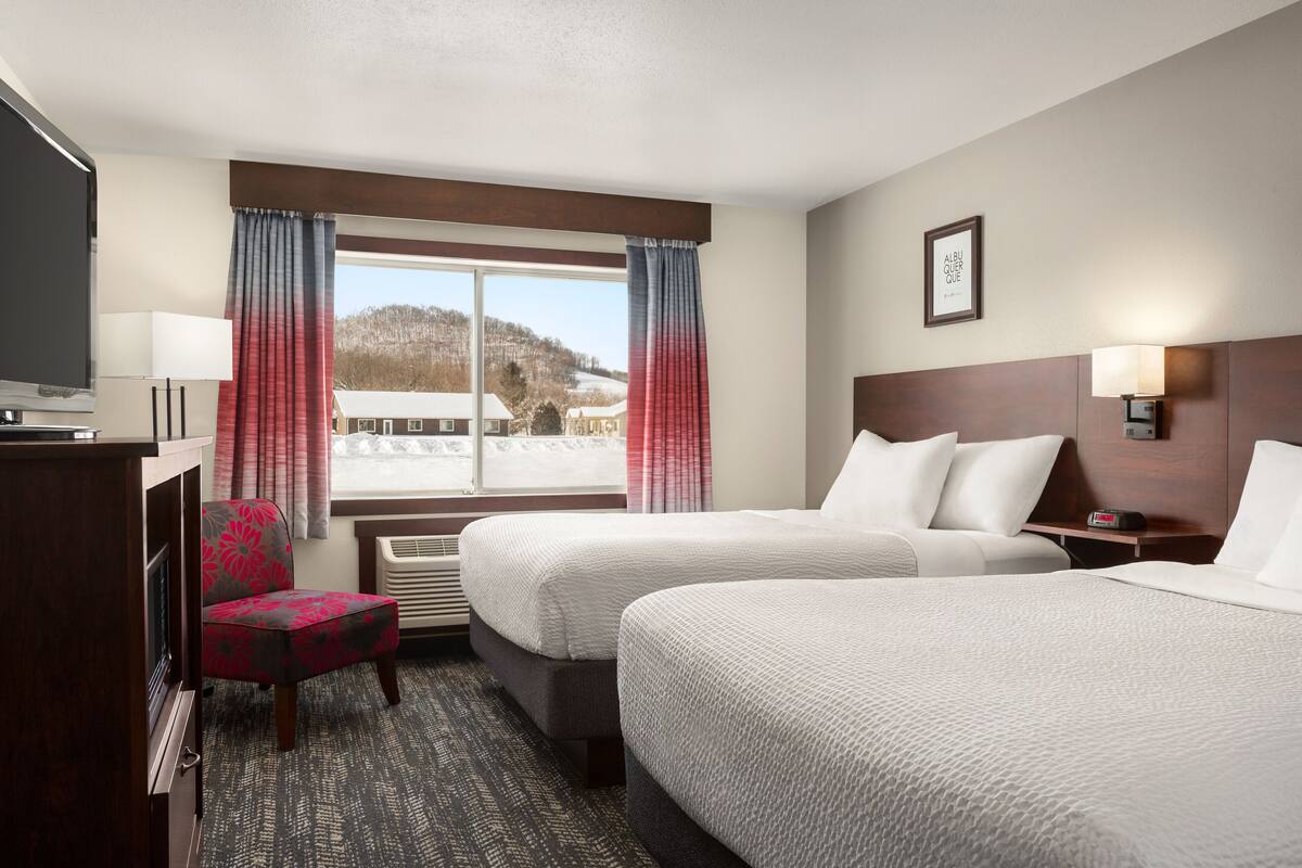 Een hotelkamer met twee bedden, een bureau met televisie, een stoel en een raam met gordijnen.
