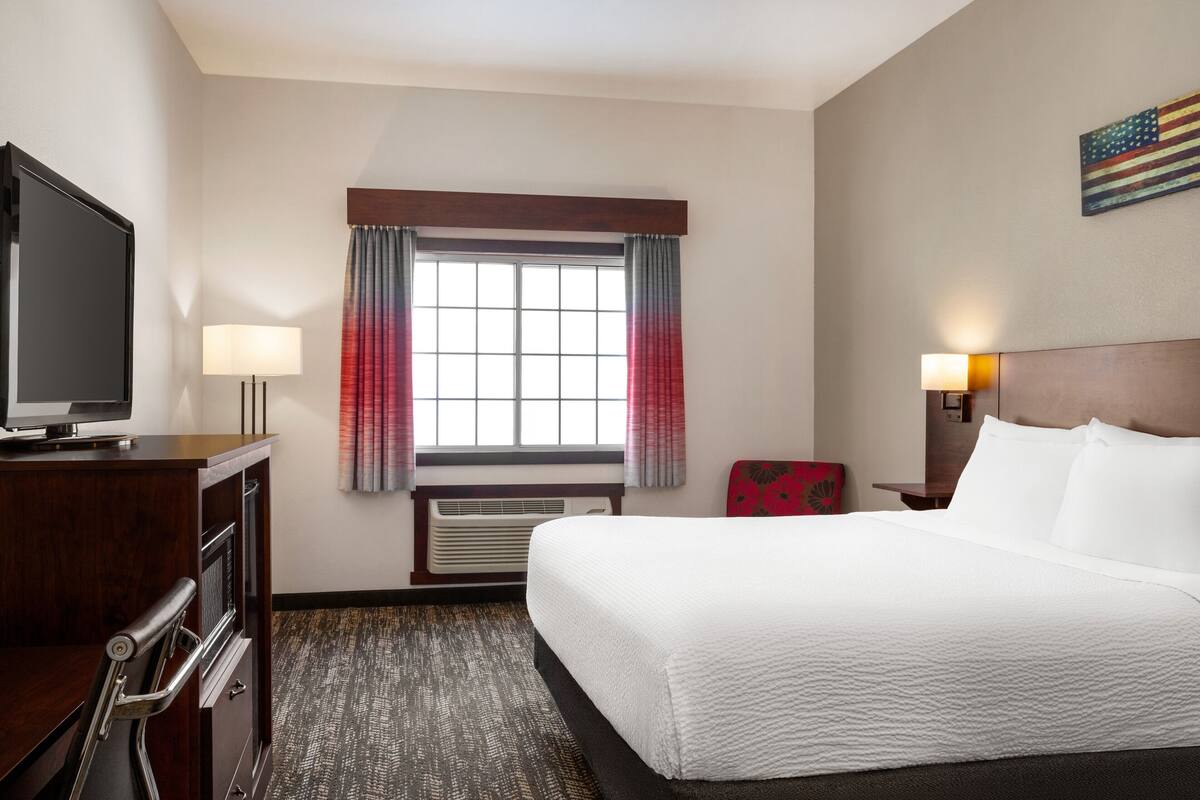 Een hotelkamer met een groot bed, een bureau met een televisie, een stoel en een raam met gordijnen.