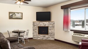 A living room with a fireplace, a flat-screen TV, a ceiling fan, and a dining area with chairs and a table.