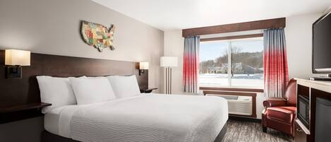 Habitación de hotel con una cama grande, un escritorio con televisor, una silla y una ventana con cortinas.