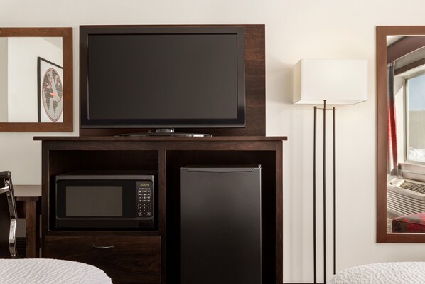 Habitación de hotel con televisión, microondas y refrigerador integrados en un mueble de madera.