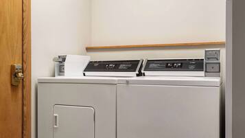 A compact, modern laundry room with a built-in washer and dryer, a wooden shelf above, and a door with a brass handle.